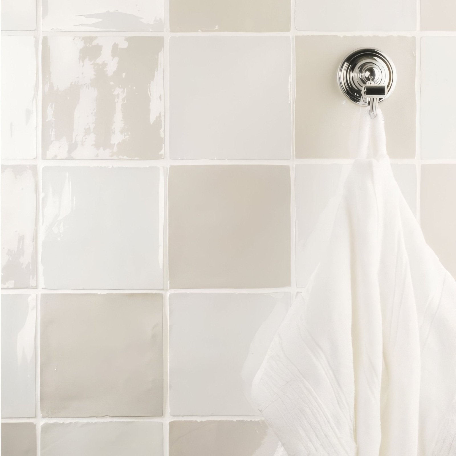 A sleek chrome towel hook with circular base and curved arm holds a white towel on a hibiscus field tile wall