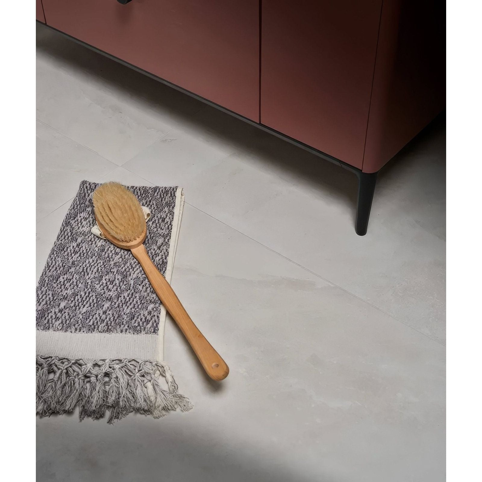 A natural wood-handled bath brush with light brown bristles on a gray and white towel from himalaya porcelain matt crystal