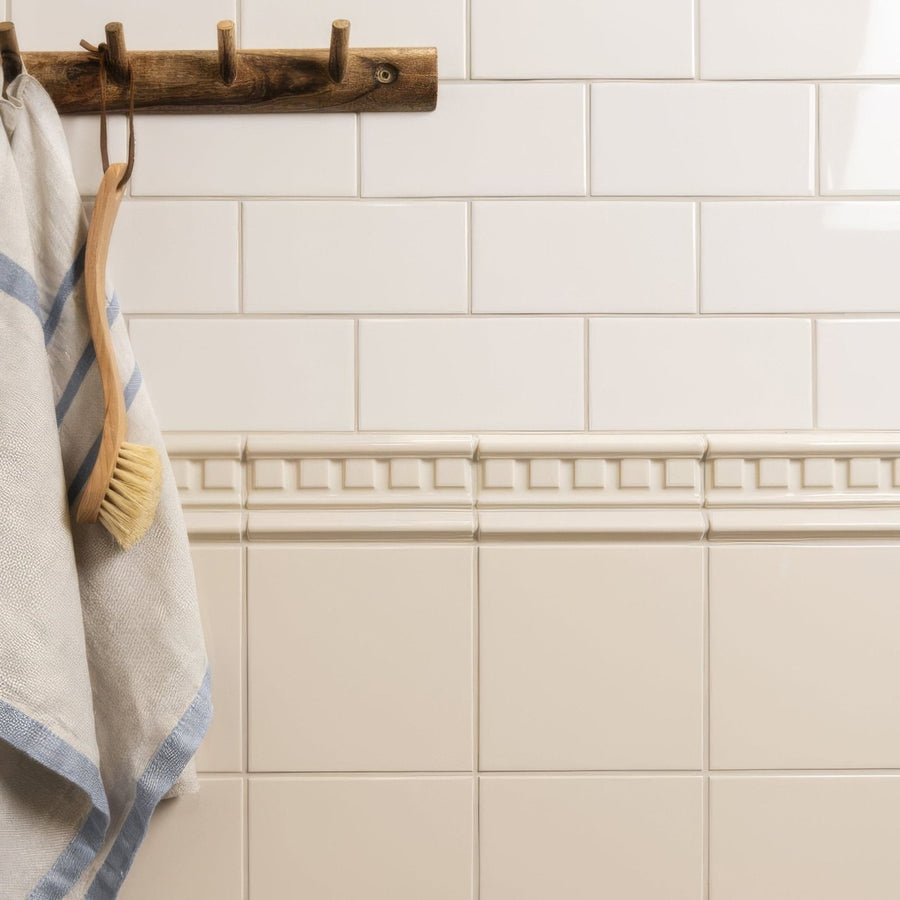 Ivory field tile cream-colored ceramic tile with a decorative raised geometric border running horizontally on wall