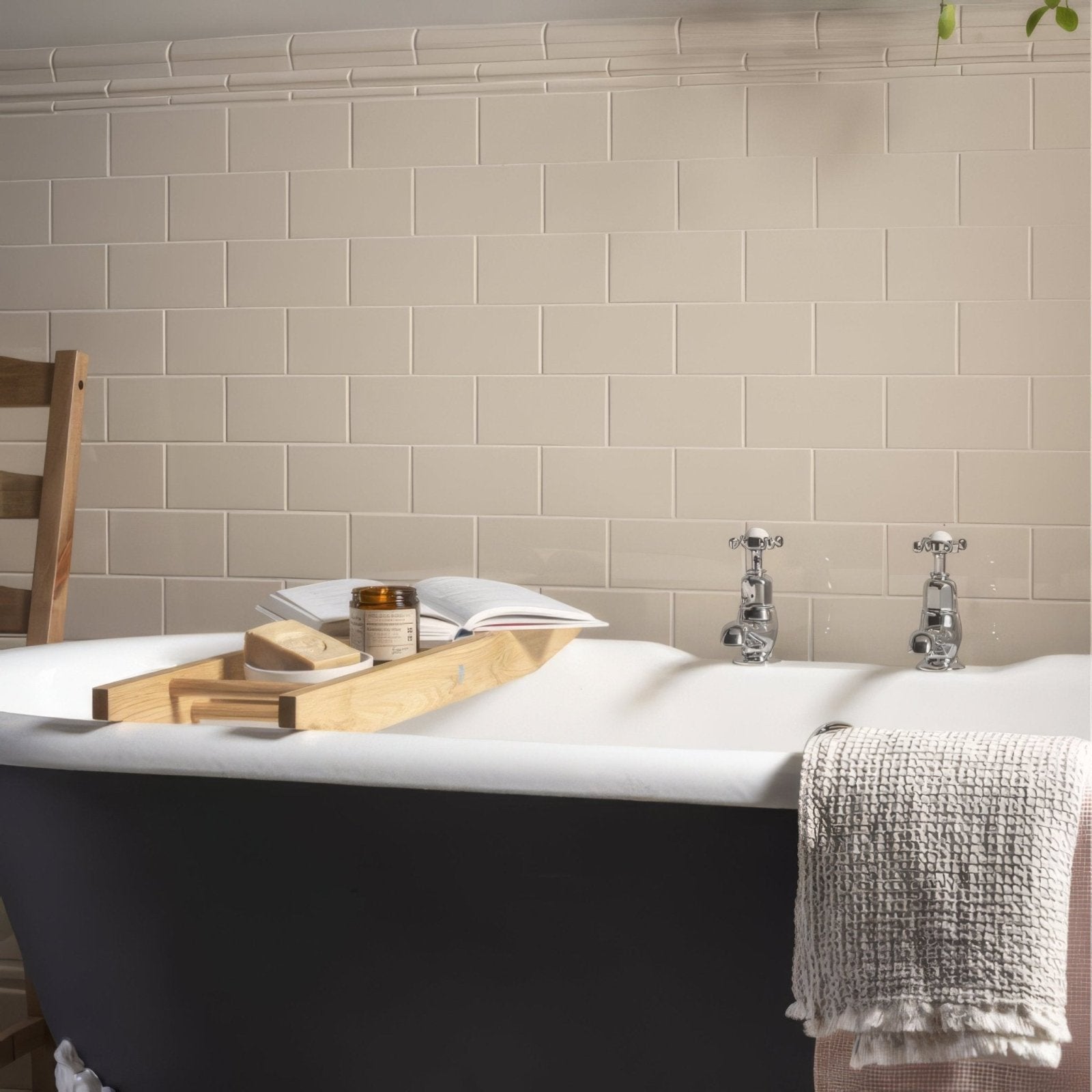 A sleek black clawfoot bathtub with white interior and chrome faucets draped in gray towel shown with ivory half tile