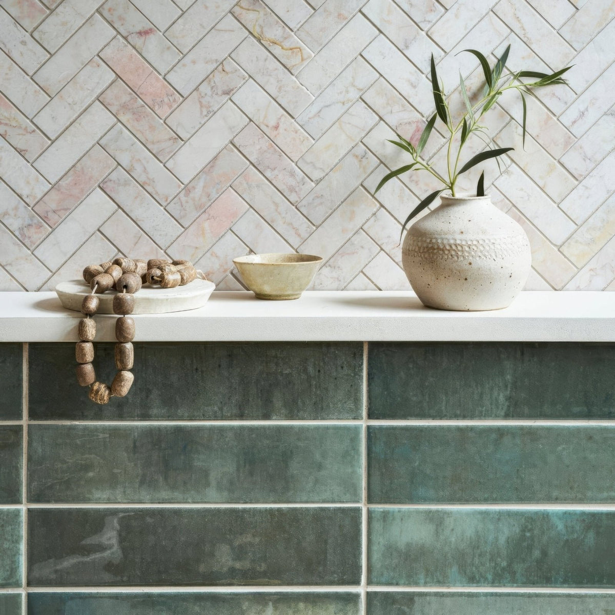 A textured off-white ceramic vase with speckled finish and embossed pattern holding green leaves beside an ixworth forest brick tile