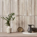 A white speckled ceramic vase with a geometric faceted design holding green eucalyptus branches on ixworth ivory bar tile