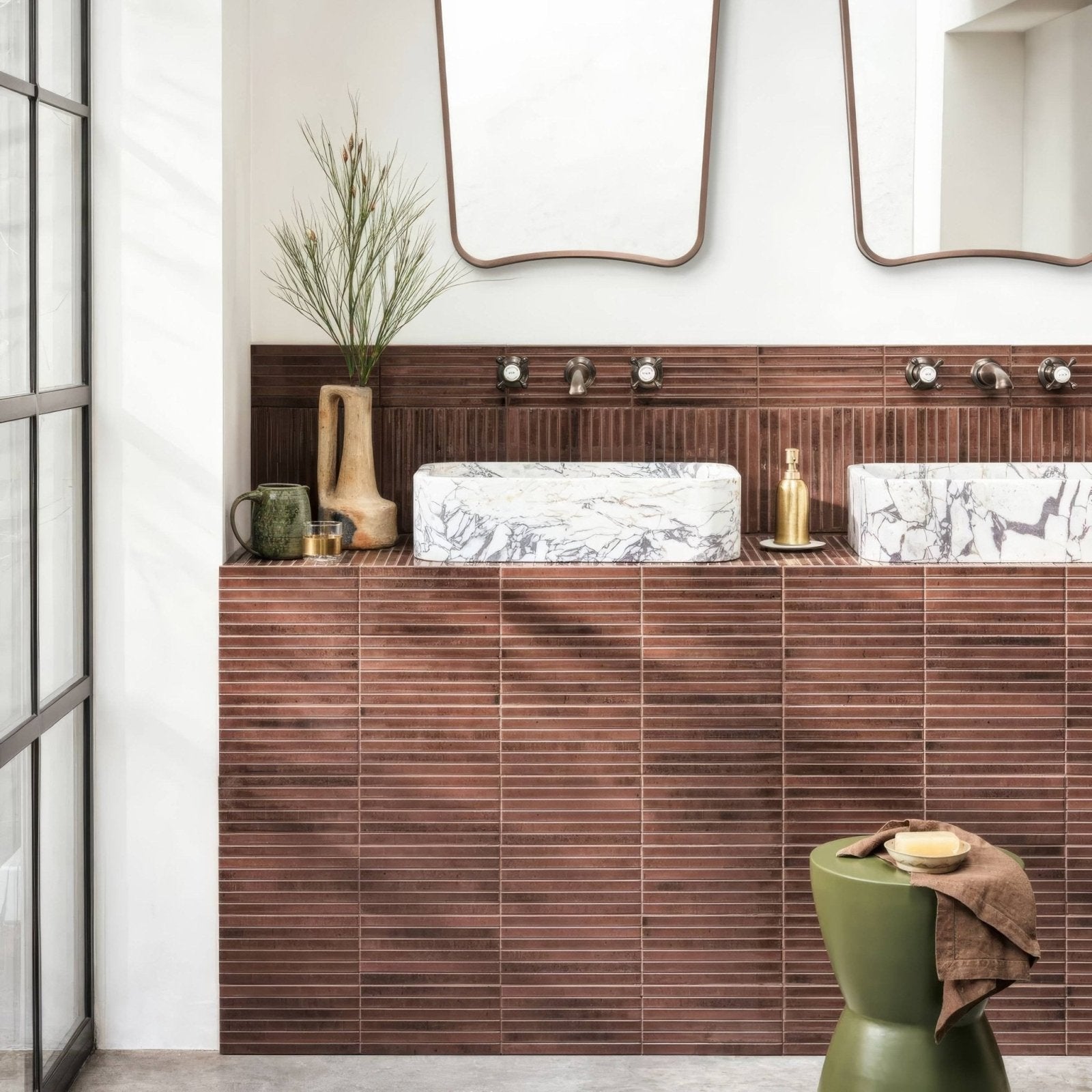Two rectangular marble sinks with gray veining sit atop a wall of horizontal copper-toned ixworth mulberry bar tiles