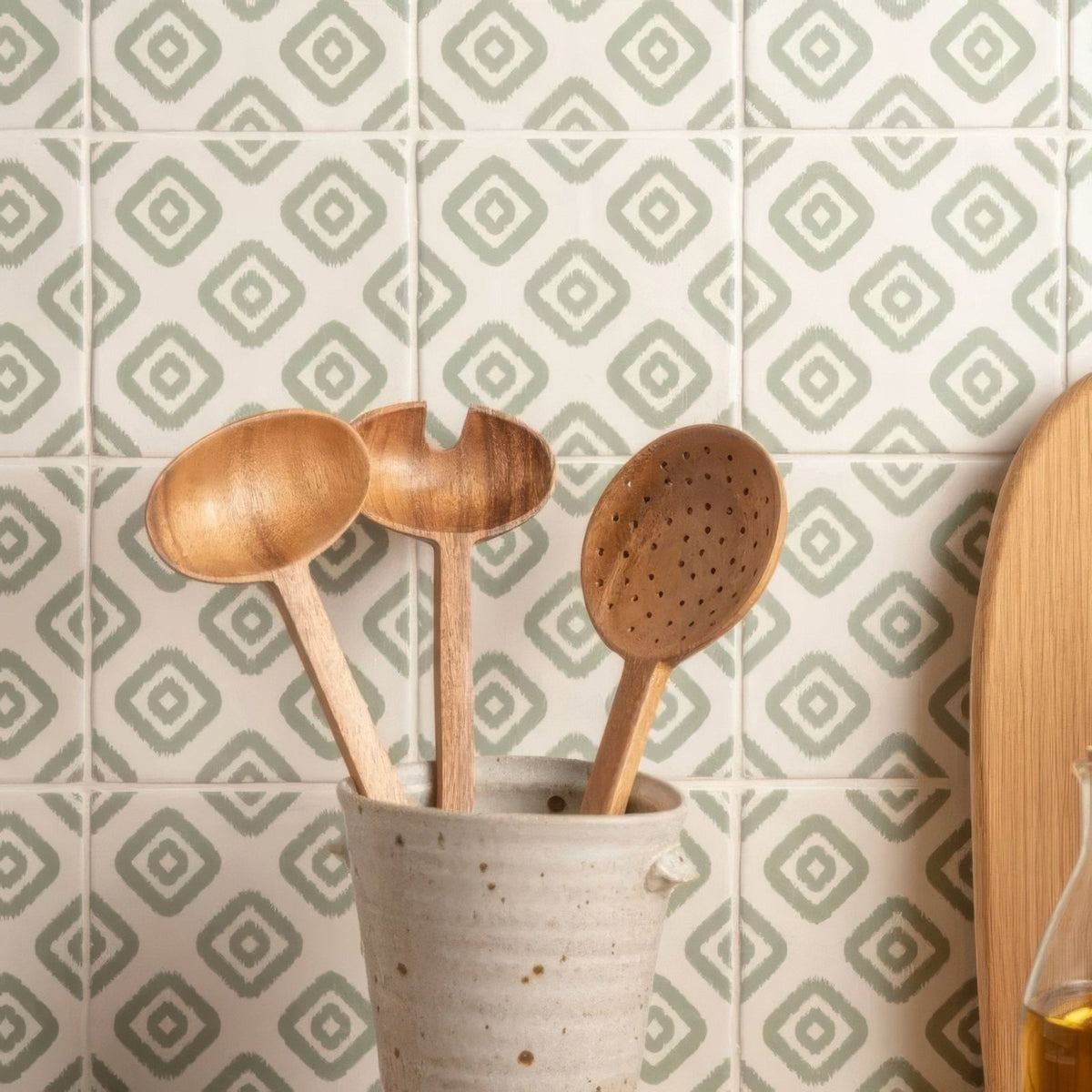 Jacquard sage three wooden spoons with natural wood grain in a speckled beige ceramic utensil holder