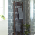Brown heated towel rack with multiple horizontal bars holding two gray towels in front of jaipur dartmouth green tile