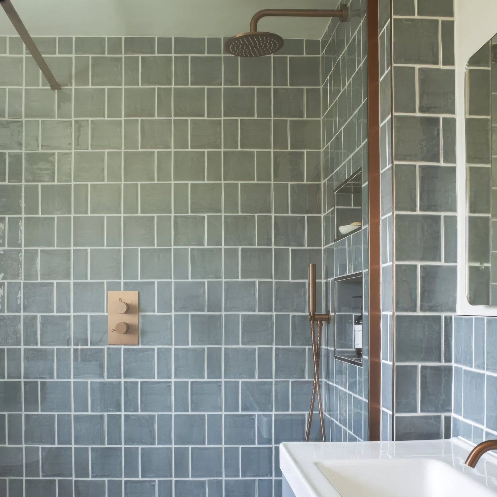 Jaipur Dartmouth green square glazed tile shown with a round bronze finished textured showerhead with spray nozzles