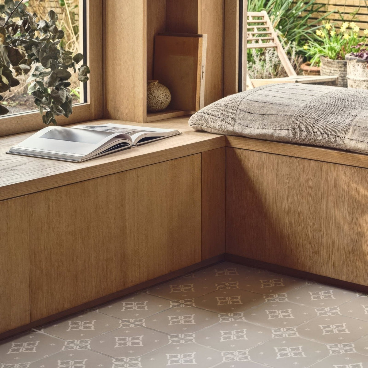 A cozy wooden window seat with a textured gray cushion and an open magazine beside jaipur sagar patterned tile