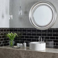 Round silver-framed mirror hung on a wall of Jet Black Half Tiles