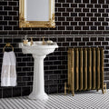 White ceramic pedestal sink with gold-toned faucets and ornate mirror above jet black skirting tile wall