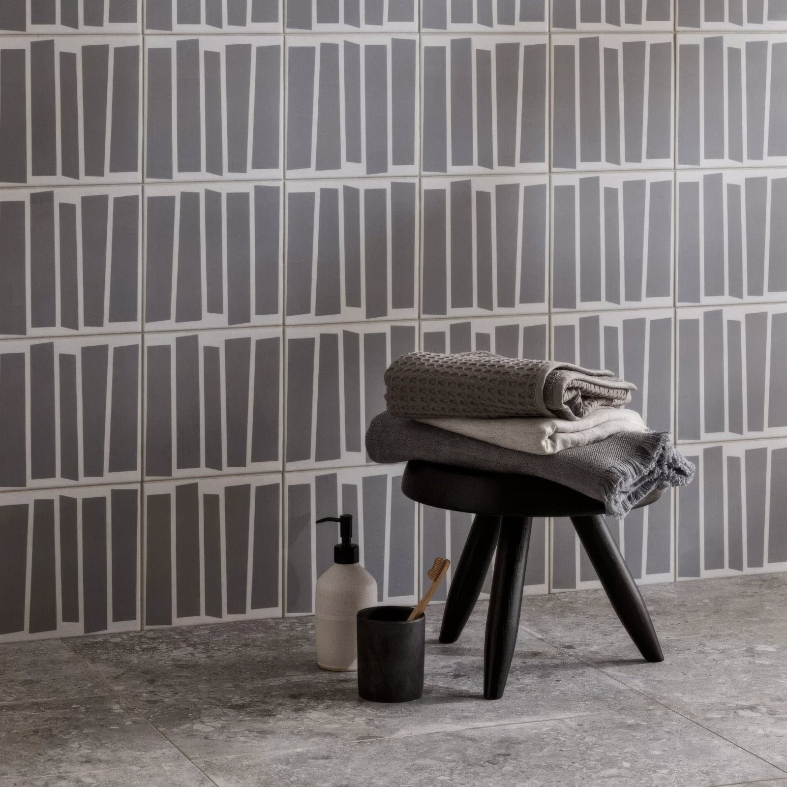 Stack of folded gray and white textured towels resting on a black three-legged stool from kelly hoppen strip black and white collection