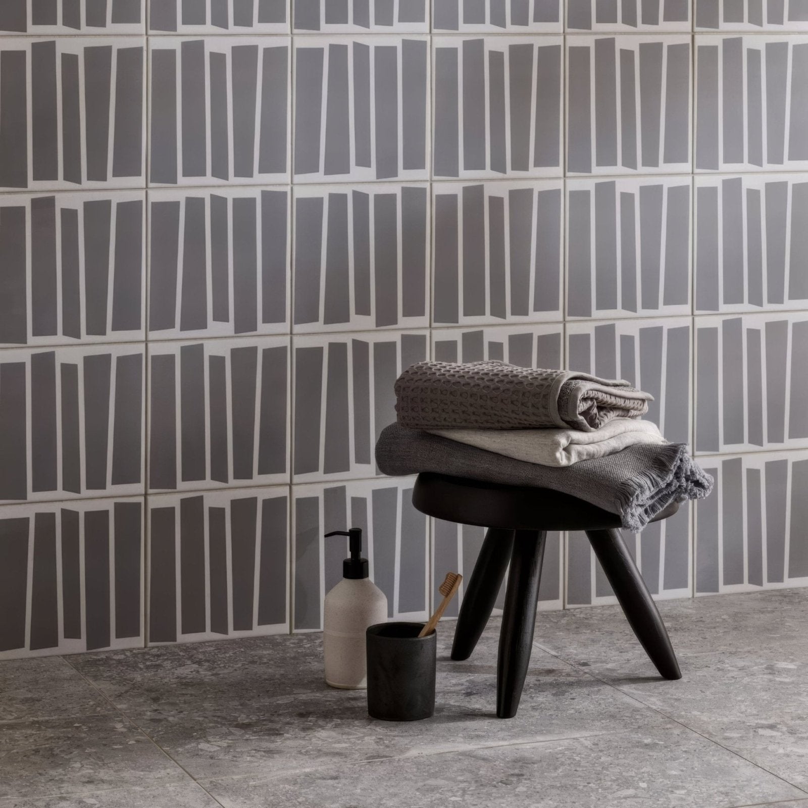 Stack of folded gray and white textured Kelly Hoppen strip towels resting on a black wooden stool