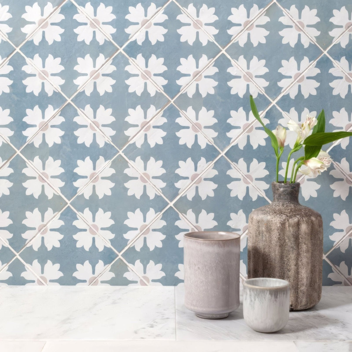 Rustic textured ceramic vase with matte grayish brown finish holding white flowers on Kelmscott Coleton blue patterned tile