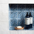 Two dark blue glass bottles with black pumps and land & water labels on kelmscott emery blue patterned tile shelf