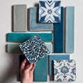 A hand holds a kelmscott emery blue patterned ceramic tile with dark blue leaf designs on a white background