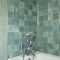Antique-style chrome bathtub faucet with white ceramic handles and flexible hose against kelmscott green tile walls