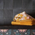Stack of folded mustard yellow and cream towels with pink floral patterns made from soft cotton for kelmscott slate black tiles