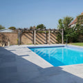 Rectangular pool with vibrant blue water and kimmeridge limestone etched bullnose coping tiled edge in paved backyard