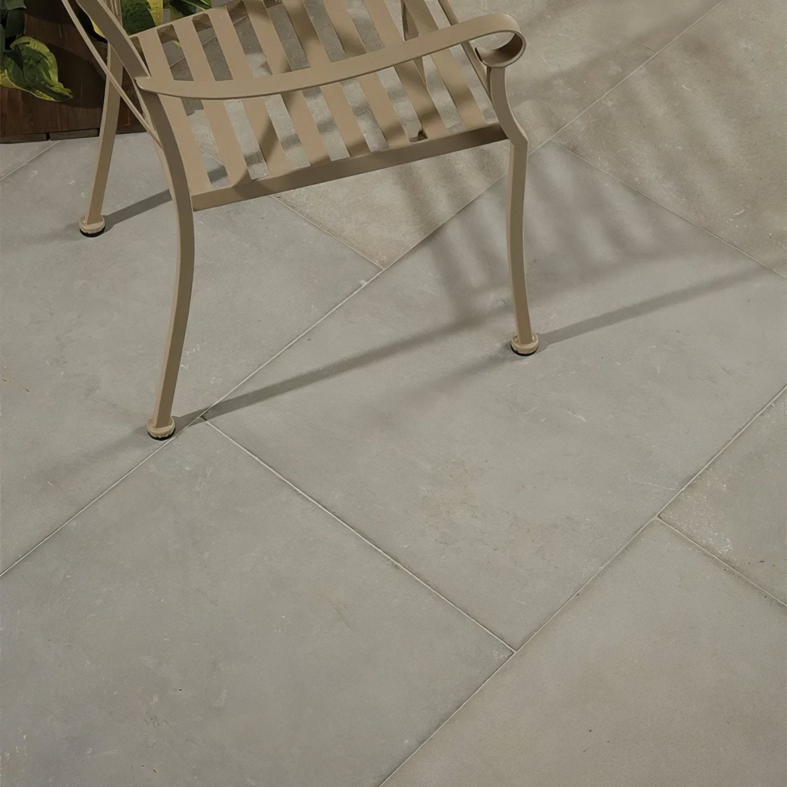 Beige wrought iron patio chair with curved armrests and slatted back in kimmeridge limestone etched finish