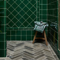 A rolled green and white striped towel resting on a wooden stool next to kimmeridge limestone tumbled and etched parquet