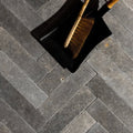 Black plastic dustpan with wooden-handled broom with natural bristles on kimmeridge limestone tumbled and etched parquet
