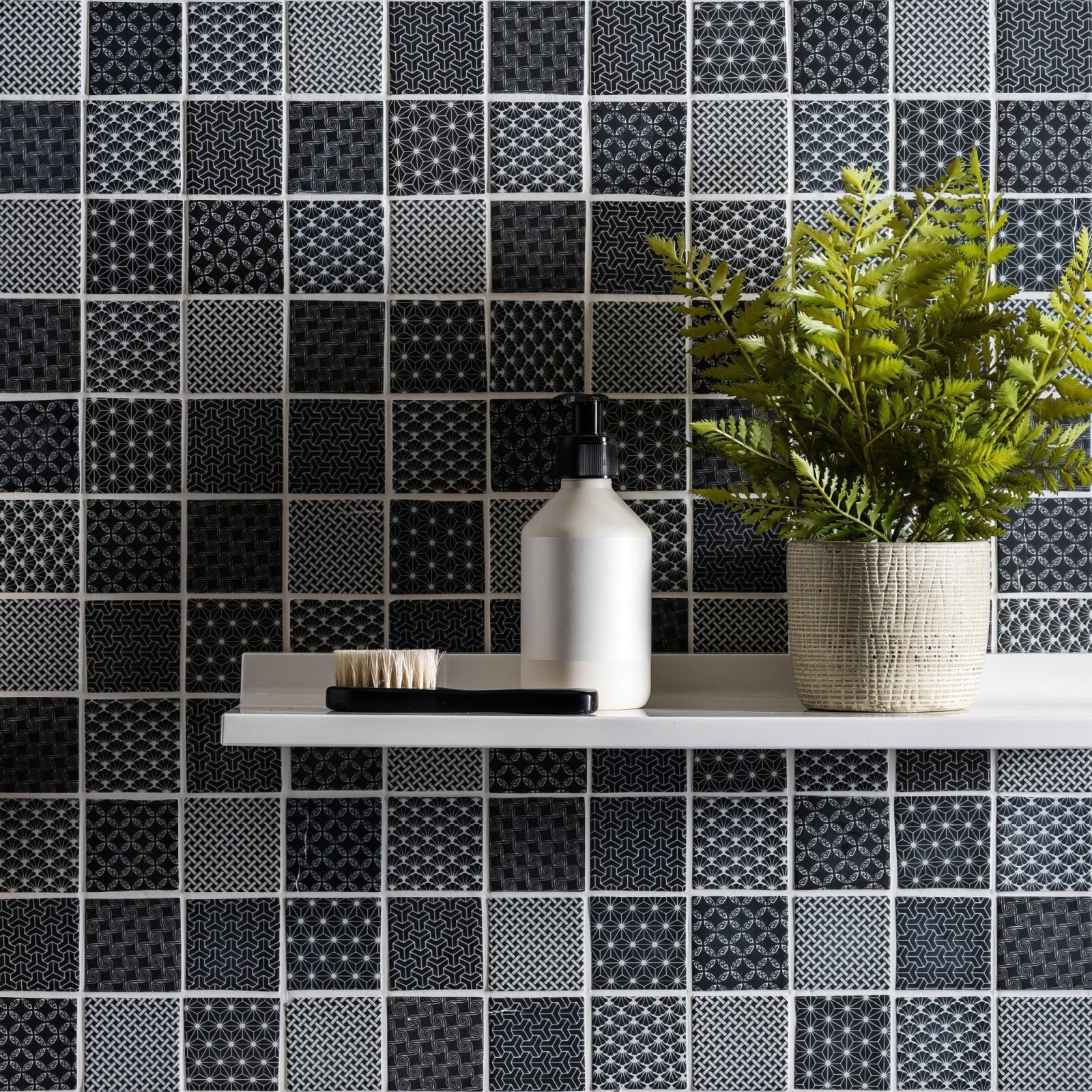 White ceramic soap dispenser with black pump on shelf against black and white mosaic tiles for kinetic black recycled glass