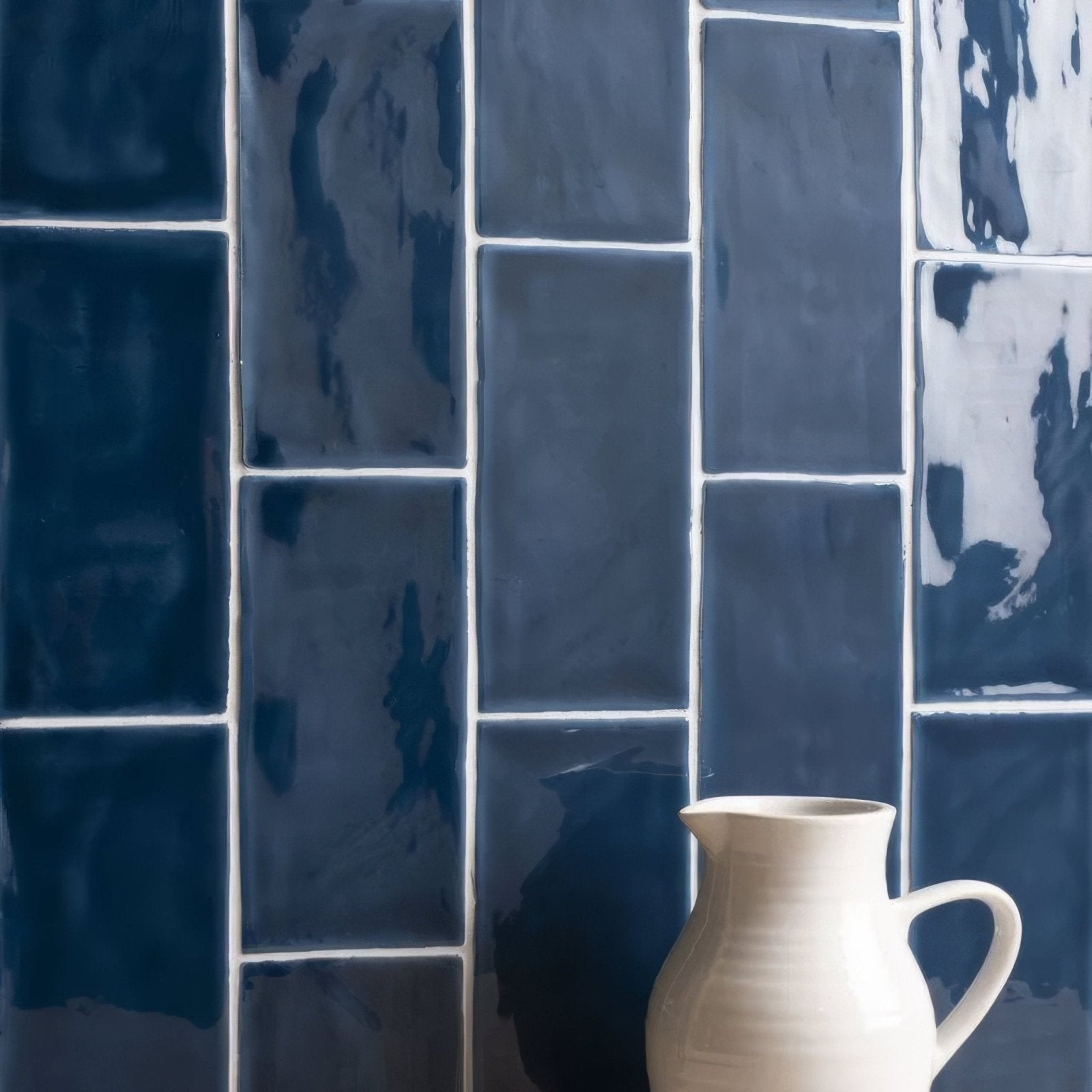 Cream-colored ceramic pitcher with a smooth textured surface and curved handle featured in lapis brick tile setting