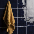 A mustard-yellow textured towel with a woven pattern hanging against dark blue lapis field tile wall