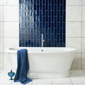 White freestanding bathtub with chrome faucet against navy blue lapis large brick tile wall background