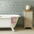 White clawfoot bathtub with pink woven towel draped over edge featuring lazul torus moulding design