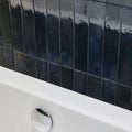 Dark blue glossy rectangular Lisbon blue cobalt shine tiles with subtle gradient and texture behind a white bathtub