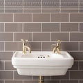 White ceramic sink with gold toned faucets installed on london stone half tile wall for bathroom use