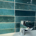 Modern chrome faucet luminous lume blue with sleek curved design against teal ceramic tile backdrop