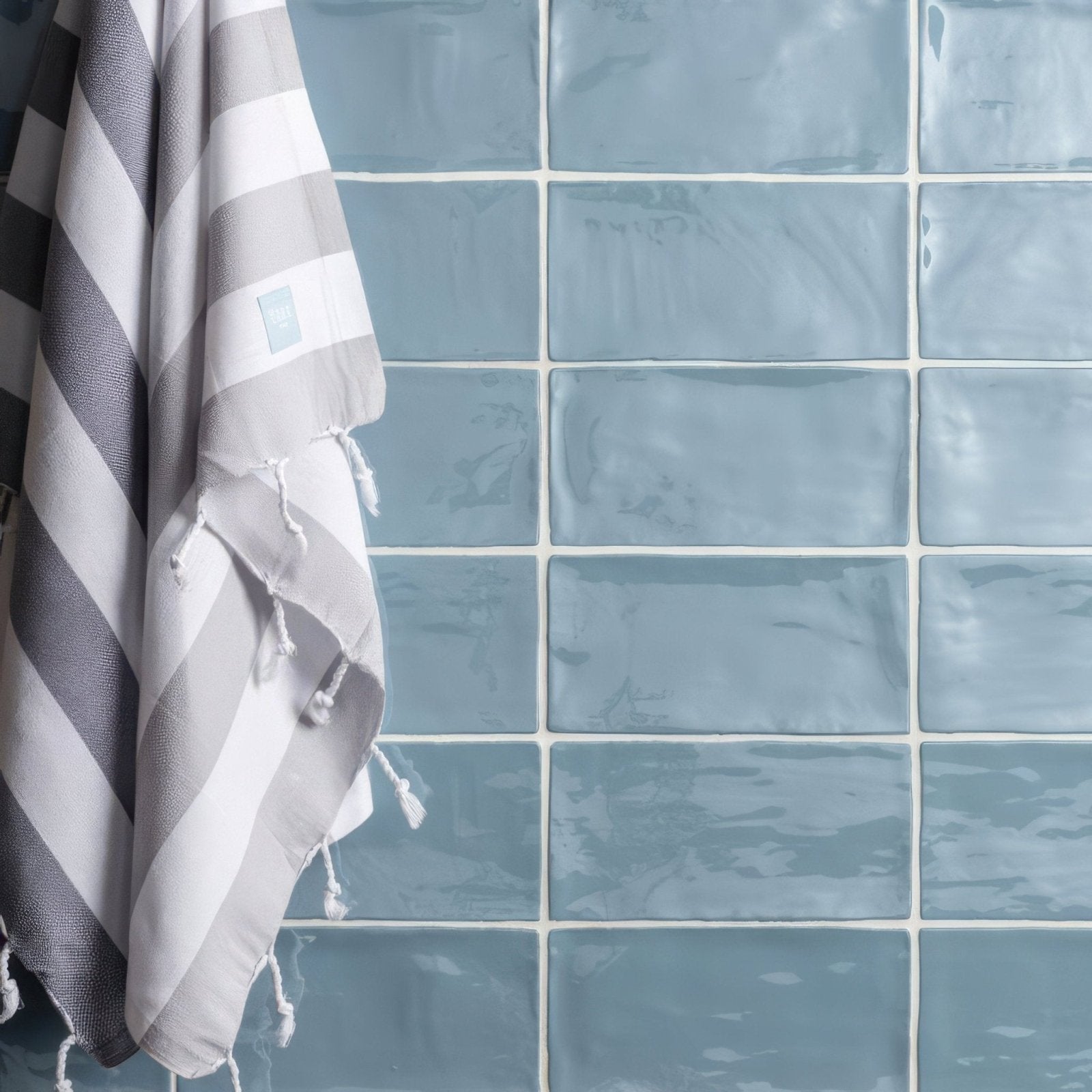 A gray and white striped towel with tassels hanging against a blue lupin brick wall tile 20x10cm background