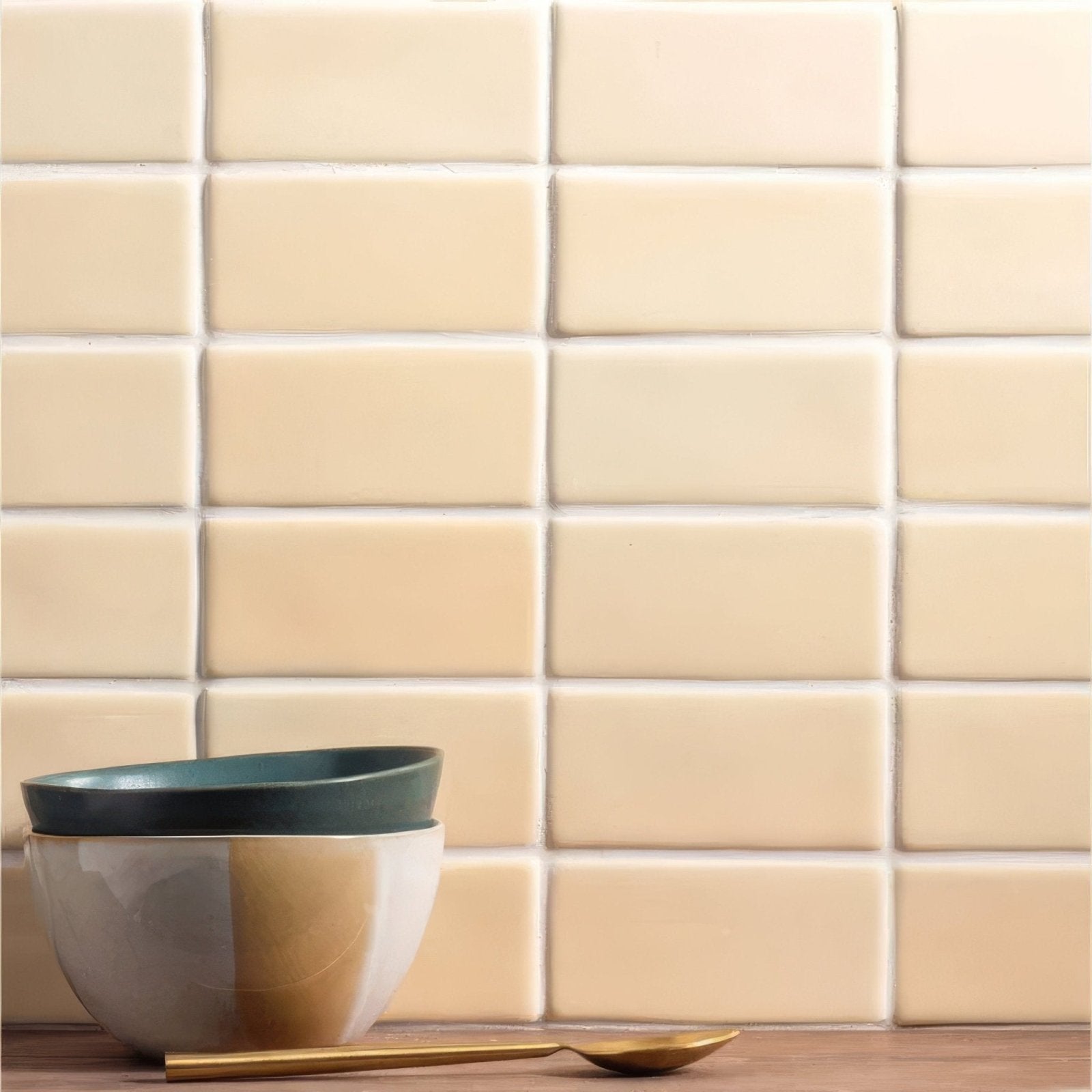 Stacked maize half tile ceramic bowls with matte dark green rim and two-toned beige and muted gold body beside golden spoon