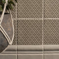 Beige ceramic tiles with a repeating dark brown geometric floral pattern from manoir provence pumice collection
