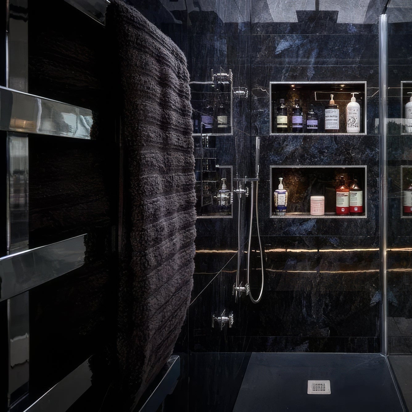 Modern bathroom with dark tiles in Marble Ocean Rock 60 x 120cm, glass shower enclosure, and shelves with bottles.