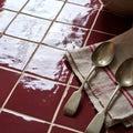 Two antique-style silver spoons resting on a beige linen napkin with red stripes for maroc ceramic bordeaux setup