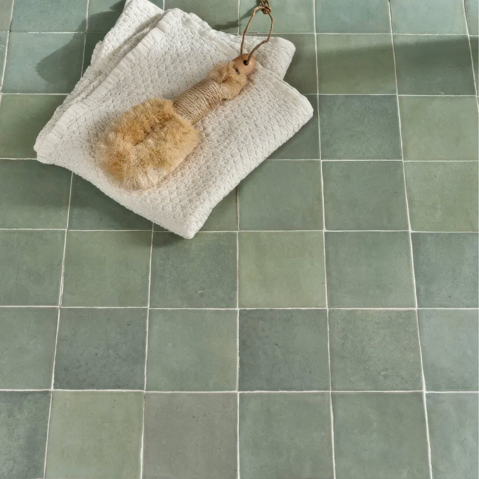A natural fiber maroc ceramic mint bath brush with a textured light brown handle and soft beige bristles on a white towel