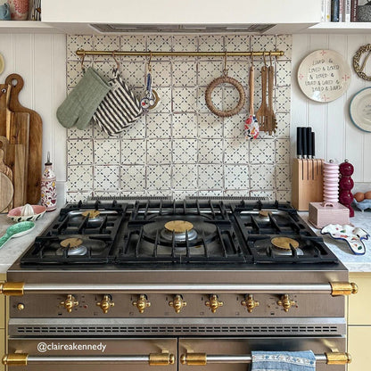 Stainless steel gas range with brass accents and gold-colored knobs featured with marrakech el hara patterned terracotta tile