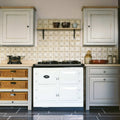 White aga range cooker with black trim and classic oval logo featured on patterned terracotta tile background