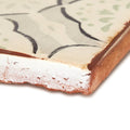 A rustic cream ceramic Marrakech Menara patterned terracotta tile with black and light green floral designs and exposed edge