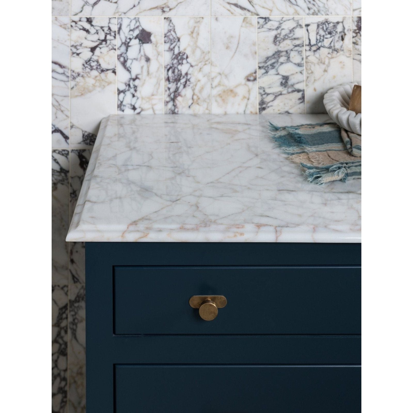 Medici Viola Marble Honed Brick white marble brick tiles with a dark teal cabinet and brass pull