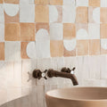 Bronze-finished wall-mounted faucet with cross-shaped handles and curved spout paired with medina raw square handmade moroccan zellige tile