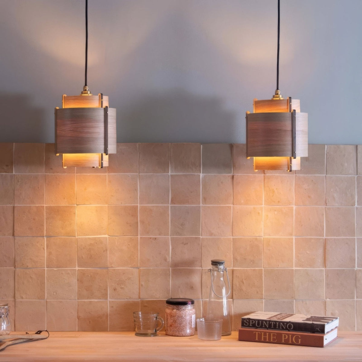 Two warm-toned rectangular pendant lights with wooden and metal accents hang above a tiled medina raw square handmade moroccan zellige tile countertop