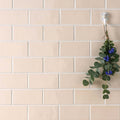 A delicate arrangement of eucalyptus leaves and blue flowers hangs on a white hook against beige melford half tile