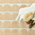 A cream-colored knitted towel and beige bath brush resting on a rustic wooden stool in menara cotto arches porcelain