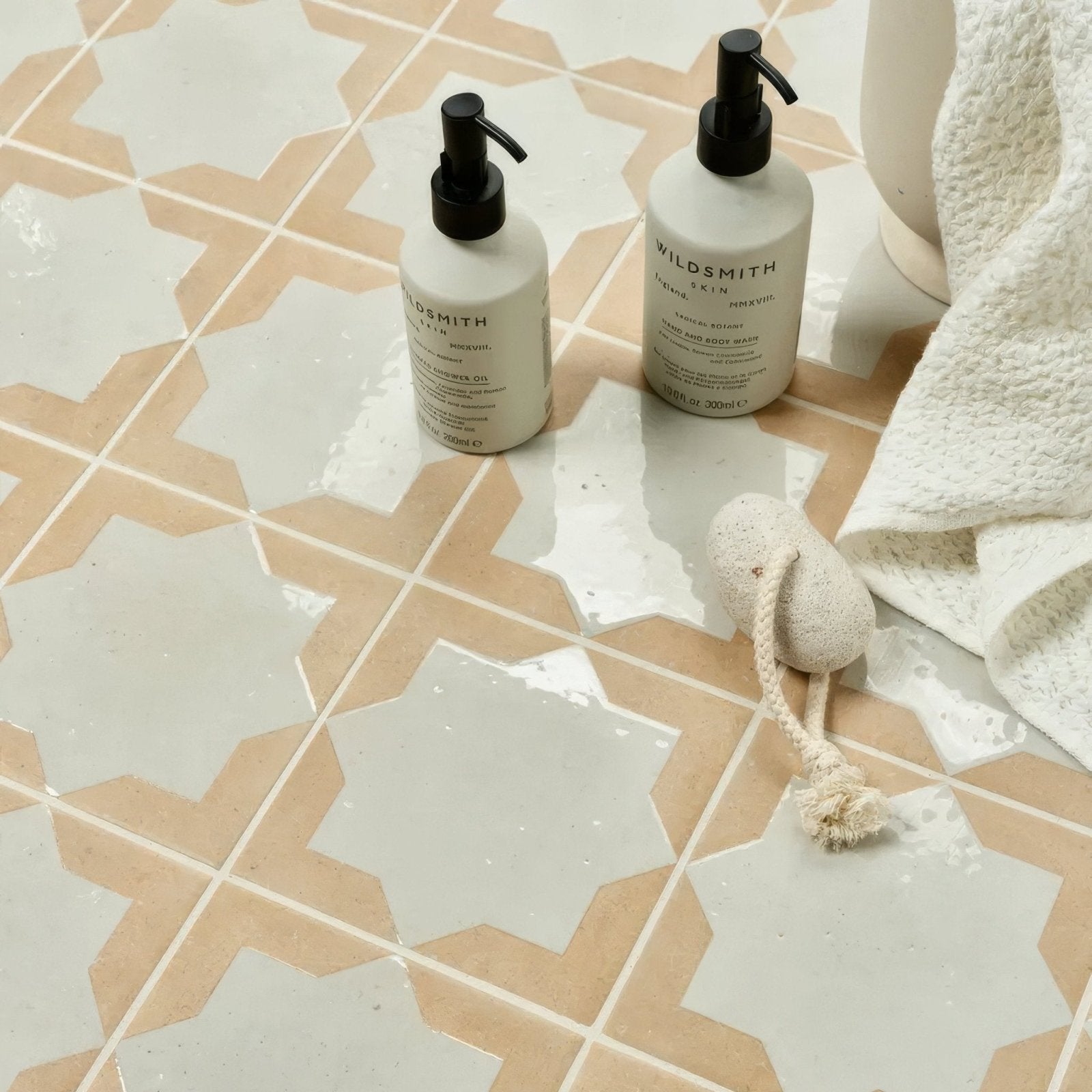 Two white wildsmith skin pump bottles with black caps on menara white star porcelain patterned tile floor