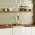 Gold-toned kitchen faucet with curved spout and cross-handle design featured in mere field tile product