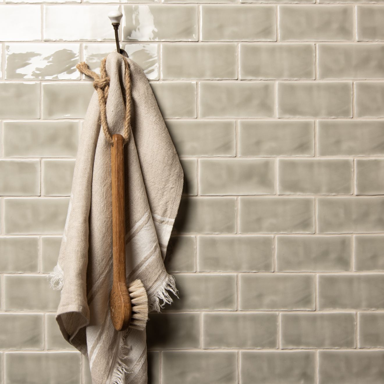 Beige linen towel with frayed edges hanging from wooden-handled brush on mere half tile wall tiles