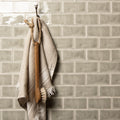 Beige linen towel with frayed edges hanging from wooden-handled brush on mere half tile wall tiles